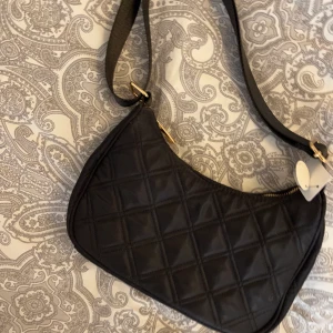 Svart väska  - Säljer denna svarta oandvända väska från Lindex (prislapp kvar) har även guld detaljer och går att ljusters bandet längre eller kortare 