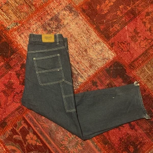 Carpenter pants - Ascoola Carpenter pants av märket sweet skbts dom har coola detaljer, i mörk blå färg, dom har coola detaljer som den vita stickningen och och fickorna på sidan, dom är i perfekt skick förutom heldragen på botten av byxan som verkligen är minimal.