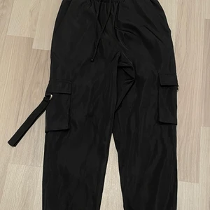 Cargopants - Svarta cargopants med fickor på benen. Något glattare material,  superskönt!  Aldrig använda.  Storlek XS