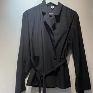 Arket blazer topp - Svart blazertopp från Arket med knytning i midjan, vida armar och fickdetalj. I kuproblanding. Helt oanvänd. Nypris 900kr.