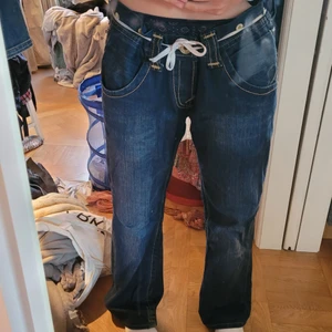 Lågmidjade True Religion jeans - Blåa baggy jeans från true Religion. Skit snygg baggy fit. Lågmidjade! Coola detaljer. Blått tyg med gula sömmar. Jätte sköna. Nice passform. Herr storlek 36. Jag har M till L i byxor. Passar deflesta men skärp kan behövas! 48cm i midjan, 73cm inner benet