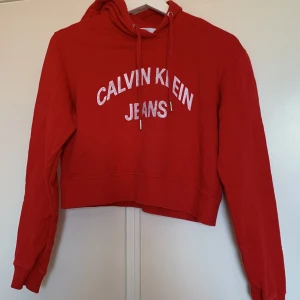 Calvin klein hoodie - Röd croppad hoodie från calvin klein. Texten på hoodien är sliten från tvätt. nypris låg runt 900 men säljer den för 200 då den är rätt så använd