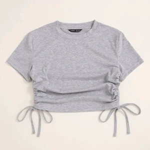 En grå crop top - Lite tajt i armarna. Man kan ändra längden på den i snörena.