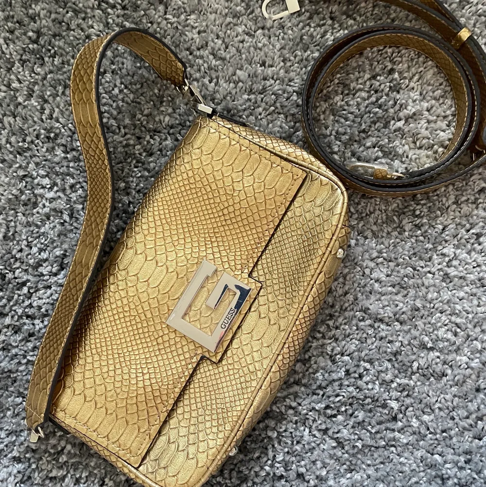 Guld väska med ormskinns mönster, aldrig använd. Från Guess! Kort band och lång band medföljer. Kan skicka eller mötas upp i Stockholms området . Väskor.