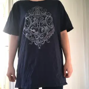 Mörkblå t-shirt med silvrigt hogwarts tryck. Köpt på sci-fi bokhandeln.  T-shirten är i begagnat skick men inte väldigt använd. Den är gjord av 100% bomull och är i storlek L.