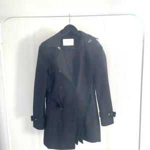 Zara kappa/trenchcoat  - Kappa från Zara i storlek S.  Avsedd för Höst/Vinter Aldrig använd.  Färgen är marinblå/svart Materialet är lätt att torka av. •Justerbar midjeband. •Knappar utanpå och innanför för att hålla värmen. •Hake upptill för att täta värmen. •Justerbara band vid