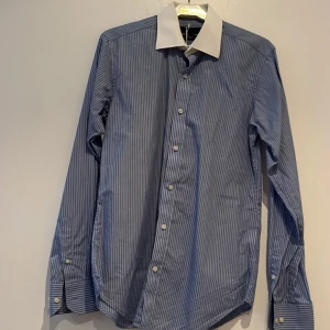 Business skjorta  - Snygg och lyxig skjorta. Alldrig använd. Enkel att stryka och tailored fit. Blå med vita ränder och vit grage.
