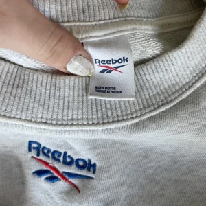 Grå Reebok tröja  - Säljer denna sjukt snygga rebook tröjan som har en vintage vibe men är helt oanvänd. Den passar perfekt nu för våren.