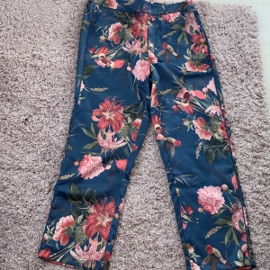 Vintage byxor  - Ett par byxor med fåglar och blommor på i bakgrunden är mörkblå 