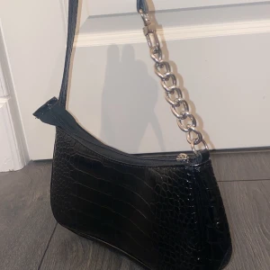 Svart väska med silver band - Säljer min svarta axelväska med silverskedja halvvägs, använd enstaka gånger. 