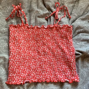 Röd-blommig topp - En röd blommigtopp i väldigt streshigt material. Den är ifrån gekås och är i storlek M. Den är för liten för mig så har inte använt den. Banden går att knyta upp och knyta hur löst eller tajt man vill.