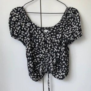 Gullig sommartop - Superfin sommartop, svart med vita blommor. Går att justera längden framtill. Resår i ryggen. Storlek M, men mer som en S.