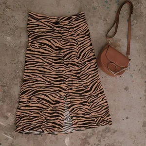 Midi kjol med tiger-print, strl 36  - Midi kjol (medellång) med tiger ränder, med knappar och slits längst ner. Är gjord i 100% viskos och tyget är lätt och andas. Knapparna går att knäppa upp hela vägen, kjolen är i bra skick och knappt använt. Obs, kjolen passar även på en storlek 38