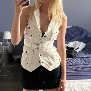 Jeansväst - Vit jeansväst med knappar där framme och ett band som gör att den går att dra ut hur mycket/lite man vill. Superfint skick❤️‍🩹