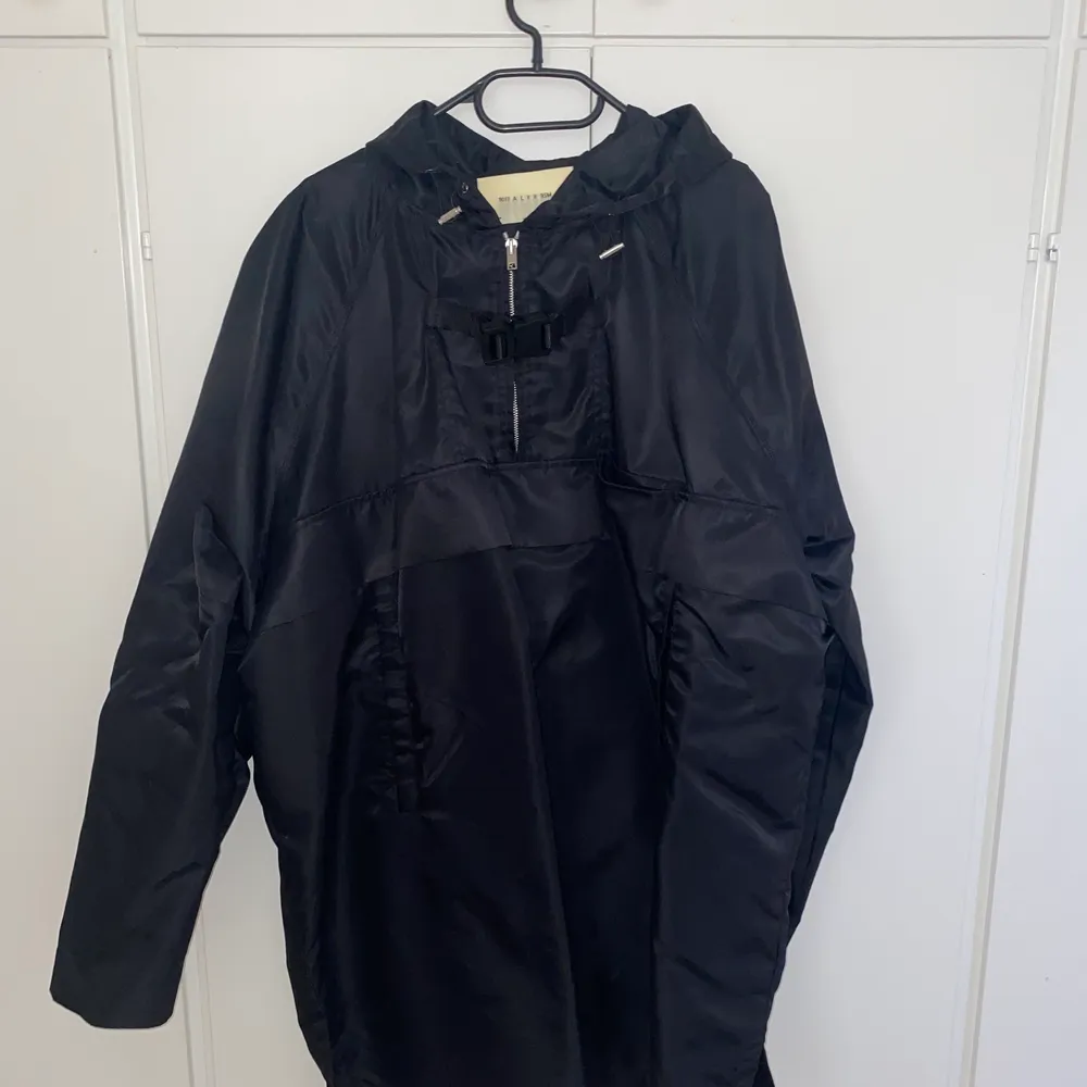 Alyx oversized rain pullover in Size L in black. In amazing condition. Features front pocket below the buckle. Only worn a handful of times. Comes with tags, sold out everywhere. Retail price is 4,488 SEK.Will ship out the same or next day.. Jackor.
