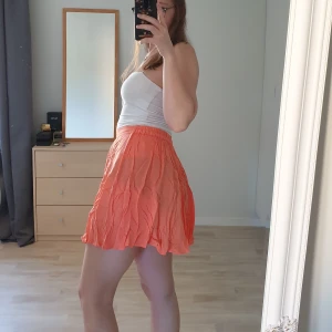 Orange kjol - Orange kjol med resår i bak för bättre passform. Lite tunnare vilket gör att svarta underkläder lyser igenom på mig, vitt fungerar bra! Även hotpants (korta cykelbyxor) fungerar bra. M, men passar även S
