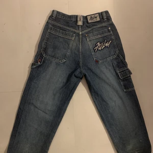 Fubu jeans - Jätte fina baggy jeans med reflex fickor och flertal fina detaljer. Använda fåtal gånger men det är köpta på humana second hand och har därför en väldigt liten slitning på framsida knä och lite vid fötterna men det är inget som är synligt. Anars är det i helt perfekt skick. Om du har frågor om mått eller fler bilder är det bara att meddela mig!  Kan fraktas och mötas i centrala Stockholm