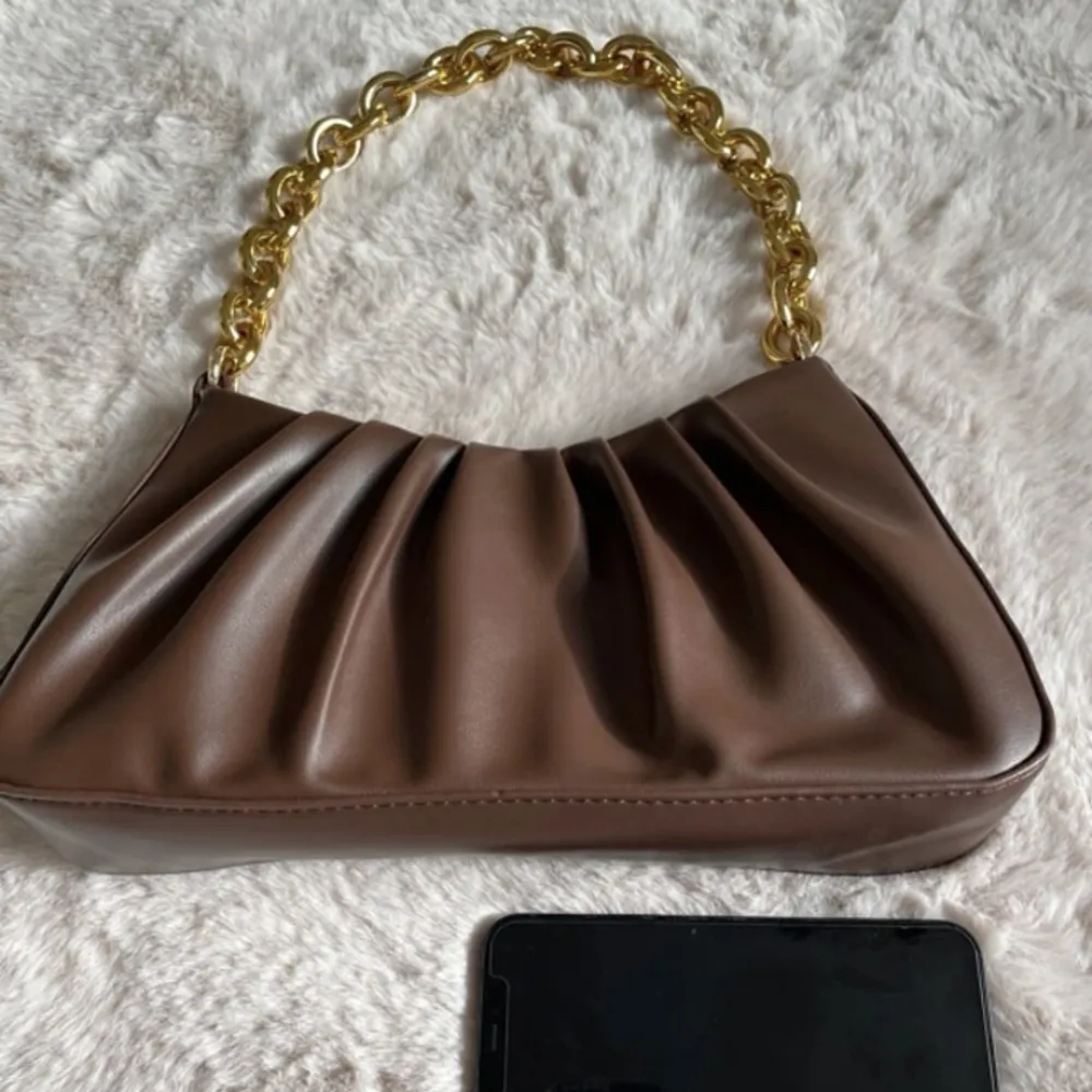 En väska som är brun med guld kedja med samettyg inuti med ett litet fack . Väskor.