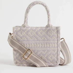 Liten handväska - Säljer denna fina lilla handväska med ett vävt material i lila & vitt! Finns både axelrem och handtag och är perfekt när man bara vill ha med sig några enstaka grejer. Mycket sparsamt använd. 