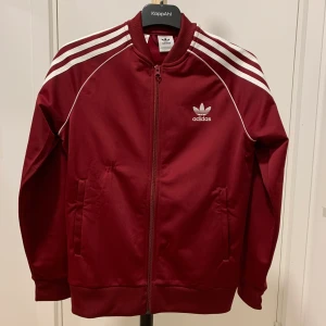 Adidas tröja - Adidas tröja i färgen vinrött. Barnstorlek 12-13Y. Passar även XS-S dam. Tröjan är i bra skick, dock finns det en liten skada på tröjan som visas i 3e bilden därav sänkt pris. 
