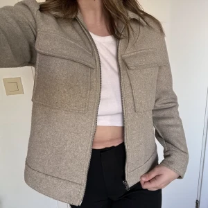 Pieces beige jacka - En beige/grå jacka is storlek M. Har två användbara fickor på bröstet. Sitter väldigt bra och är en vår/höst jacka. Aldrig använd.