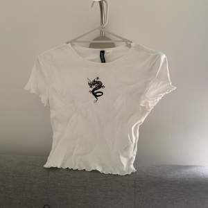 Vit croppad T-shirt med svart drak-tryck på framsidan. H&M Divided storlek S. Produkten stryks innan mötet för leverans, tid för det har inte funnits innan annonsen behövde läggas upp
