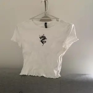 Vit croppad T-shirt med svart drak-tryck på framsidan. H&M Divided storlek S. Produkten stryks innan mötet för leverans, tid för det har inte funnits innan annonsen behövde läggas upp