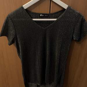En grå glittrande tröja, framsidan är kortare än baksidan 