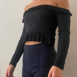 Off shoulder topp - Croppad svart off shoulder topp. På andra bilden såg jag att den nedre volangen fastnat innanför tröjan. Volangen följer hela vägen runt.