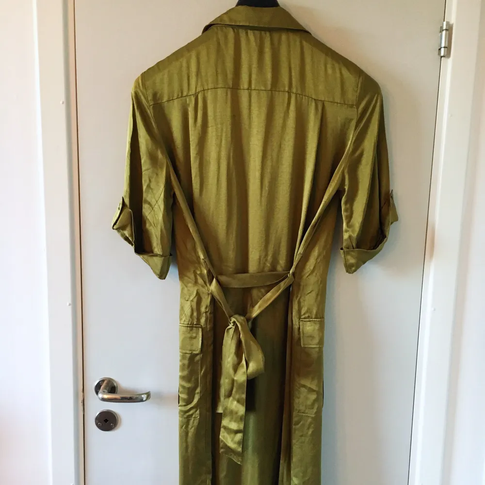 Olivgrön klänning med knäppning fram och snöre baki   Silkigt material . Klänningar.