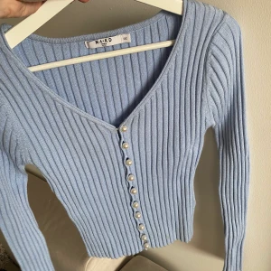 Blå ”kofta” - En blå kofta från NA-KD med pärlor som knappar. Är i storlek XXS men passar Xs då den är stretchig