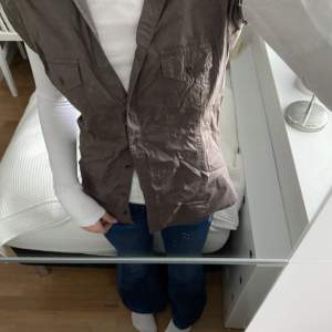 En ”skjortväst” i stilen cargo. Köpt på 90-talet i märket Slutherland. Det står storlek L på tröjan, men skulle säga att det är storlek S/M. Funkar lite som en korsett på baksidan, då man knyter den beroende på hur tight man vill ha. (Smutsig spegel)