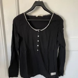 Svart topp från Odd Molly, storlek M - Fin svart topp från Odd Molly i sparsamt använt skick. Storlek 2 vilket motsvarar M/38 men jag som är S har kunnat ha den också.   Stretchig och mjuk med fina detaljer. Bland annat en rosett på ena ärmen i ljusrosa,