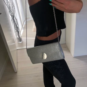Silver väska  - Liten silver väska från Tiamo. Endast använd 1 gång. Kan användas som clutch men finns en kedja så man kan hänga den på axeln. 