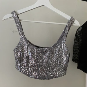 Glittertopp - Topp i glittertyg, den är sydd som en korsett, kan va lite svårt o se men sömmarna är i ett sådant mönster samt att den går lite längre ner i fram, (se bild 2)