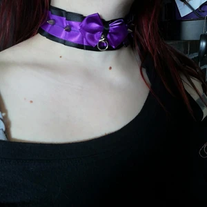Lila nithalspand  - Deta är ett lila tyg halspand med 4 silvriga små nitar och en silvrig lien metal ögla samt lila roset svart och lila tug knyts fast baktill med jälp av ett lila snöre använd 1 gånger enbart så got som ny 