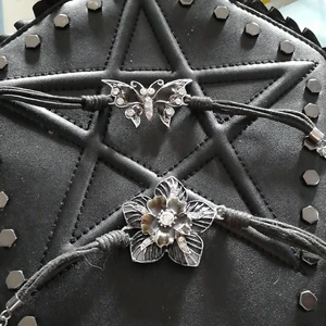 Armband blomma fjäril - Två svarta baband med glas stenar den ena i form av en svart blomma de andra i form av en svart fjäril  läder snöre och metal spene som hakas fat i skedajn på andra änden. mycke bar skid då jag knappt har använt desa alla  lite damig kanske 40kr styck eller ett paketpris vid intresse för bege 😉