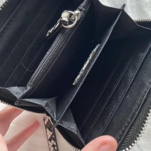 Plånbok från Don Donna - Plånbok från Don Donna i ormskinnsmönster med silverdetaljer. Använd ett fåtal gånger, ca 13x10x2cm i storlek. Får plats med 6 kort & även lite kontanter i en mindre ficka med dragkedja, se på bild. Den är hel & ren. Orginalpris 299kr, pris kan förhandlas
