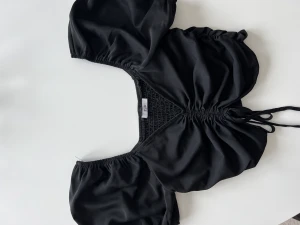 Svart topp - Justerbar hur kort man vill ha den. Har små puffarmar och risprni bak så att peroende på hur stora brost man har så kommer man i den i alla fall. Skönt material inget man svettas i den blir eller inte nopprig för materialet är inte vanligt tyg 