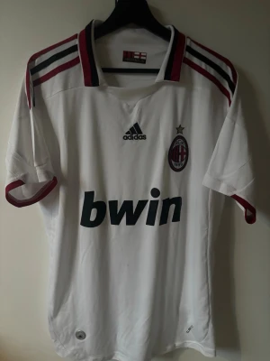 Fotbollströja ac milan - Säljer en vit AC Milan bortatröja från Adidas med klubbmärke och Bwin-logga på bröstet. Tröjan har röda och svarta detaljer på krage och axlar samt korta ärmar. Tillverkad i lätt och ventilerande material, perfekt för fotboll eller träning. Väldigt fint skick och riktigt bra kvalitet. Mycket fina broderade märken och detaljer alltså inget tryckt dåligt.