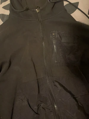 Svart hoodie från Calvin Klein Jeans kan passa S  - Säljer en svart hoodie från Calvin Klein Jeans med dragkedja framtill och huva. Hoodien har en bröstficka med dragkedja och en klassisk, enkel design. Perfekt för dig som gillar stilrena plagg med diskreta detaljer.