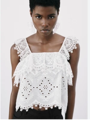 Slutsåld spetstopp med volang - Superfin vit linnetopp med breda axelband, detaljerad spets och volangkant. Toppen har broderade mönster och en luftig, croppad passform. Perfekt för varma dagar och ger en romantisk vibe till din outfit. Från zara, går inte att få tag i längre.