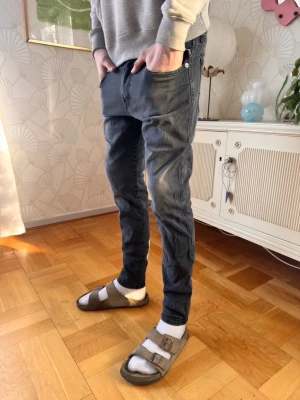 Replay ANBASS - Snygga mörkgrå slim fit jeans med klassiska fem fickor och diskreta slitningar. Jeansen har normal midja och smal passform hela vägen ner. Perfekta för en avslappnad och trendig stil. Pris kan diskuteras!