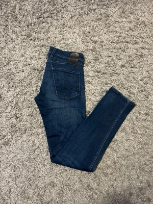 Mörkblå jeans från REPLAY - Snygga mörkblå jeans från REPLAY med diskret tvätt. Modellen är ANBASS och har en läderpatch med logga bak i midjan och stretchigt material hela vägen ner för en bekväm passform. Tveka inte på att höra av dig vid minsta fundering!