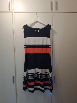 Randig klänning i bomull från Park Lane - Snygg ärmlös klänning från Park Lane med breda ränder i marinblått, vitt och en accent i korallfärg. Klänningen har en klassisk A-linjeform och är knälång med dragkedja baktill, perfekt för sommarens alla tillfällen. Tillverkad i bomull med bomullsfoder.