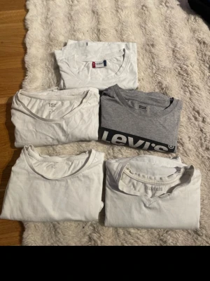 5-pack t-shirts från Levi's och H&M - Säljer ett 5-pack t-shirts i basic stil, fyra vita och en grå från Levi's med logga. Alla har rund hals och korta ärmar. Perfekta till jeans eller shorts och enkla att matcha. Märkena är Levi's och H&M. Materialet är mjuk bomull.