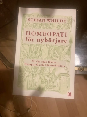 Homeopati för nybörjare bok - En bok med titeln 'Homeopati för nybörjare' av Stefan Whilde. Omslaget är vitt med gröna mönster och röd text. Boken handlar om hur man kan använda homeopati för egenvård och läkemedelslära. Perfekt för dig som vill lära dig mer om alternativ medicin.