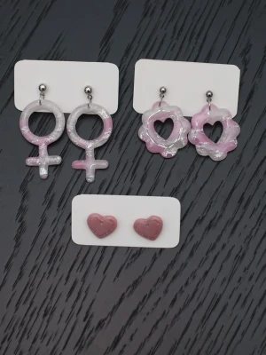 Handgjorda örhängen i polymerlera och stift i rostfritt stål feminist kvinnosymbol rosa - Handgjorda örhängen i polymerlera och stift i rostfritt stål.  Självklart nya och oanvända. Storlek: Ovala med hjärtan 2,5x3,5cm. Kvinnosymbol 2,5x5cm. Små hjärtan (stiftörhängen) 1,5x1,5cm.  Färgerna kan variera beroende på skärminställningar.