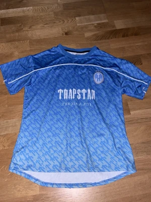 Blå t-shirt med tryck - Snygg blå t-shirt från med vit logga och text på bröstet samt stort nummer 22 på ryggen. T-shirten har ett mönstrat tryck över hela plagget, rund halsringning och korta ärmar. Perfekt för dig som gillar streetwear och vill sticka ut.