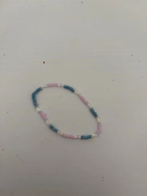 Pastellfärgat pärlarmband - Sött armband med små pärlor i pastellblått, ljusrosa och vitt. Pärlorna är trädda på elastisk tråd och armbandet har en enkel, ungdomlig design som passar perfekt till en avslappnad stil.